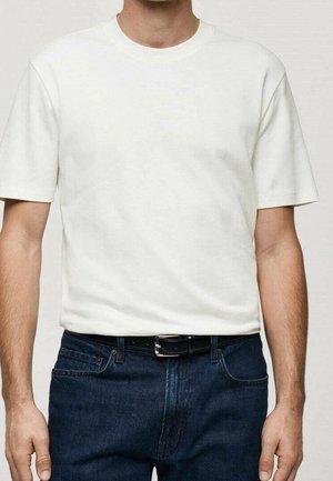 Mężczyzna w prostym białym, krótkim rękawie, koszulce z okrągłym dekoltem, włożonej do ciemnoniebieskich dżinsów z czarnym skórzanym paskiem.