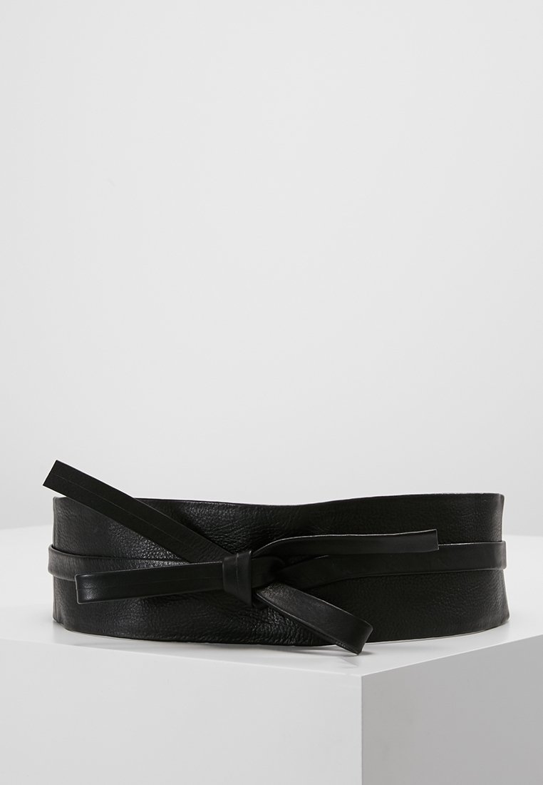 Ceinture large en cuir noir avec un détail de nœud noué sur une surface blanche sur fond uni.