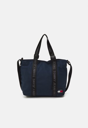 Navy blue Tommy Jeans tote bag with black double top handles and adjustable shoulder strap, featuring logo straps and a small logo patch.