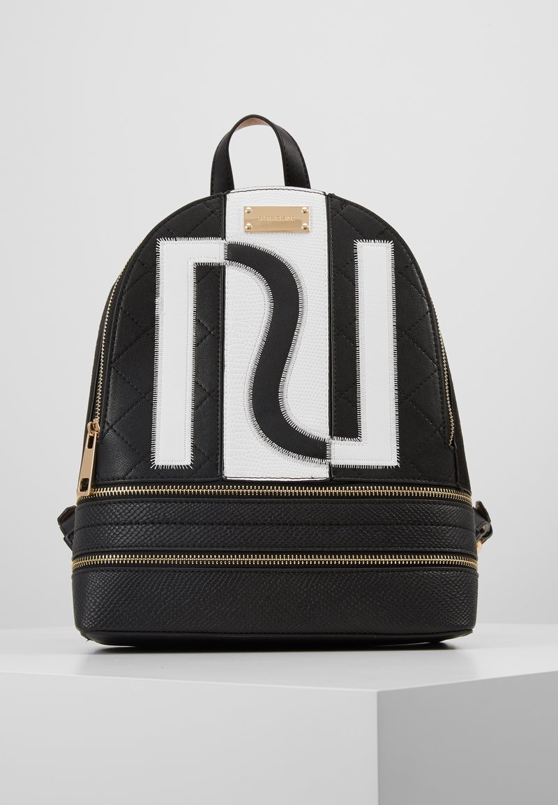 Black quilted backpack made of textured material, featuring a white logo and gold hardware, with dual zippered compartments and top handle.