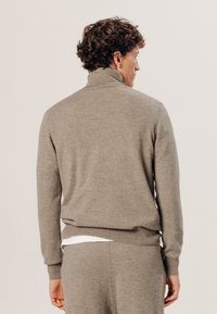 Lichtbruin, wollen turtleneck trui met lange mouwen en ribgebreide manchetten. Heeft een soepele textuur en een getailleerde pasvorm.