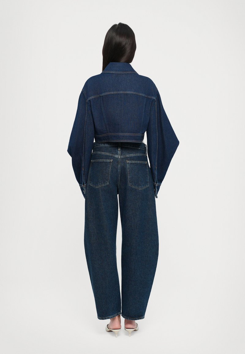 Dark blue denim cropped jacket with wide sleeves, paired with relaxed-fit dark blue jeans. Visible back pockets and cuffs.