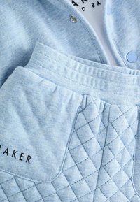 Completo in cotone di colore azzurro chiaro, composto da una camicia con bottoni e pantaloni con vita elastica, caratterizzati da un design a tasche trapuntate. Testo "BAKER" in nero.