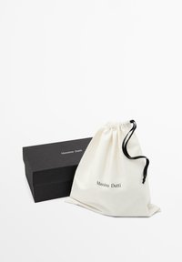 Krémový bavlněný sáček na zavazování s potiskem "Massimo Dutti" v černé barvě, vedle černé obdélníkové papírové krabičky.
