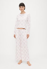 Σετ πιτζάμες με μακριά μανίκια σε λευκό ύφασμα με ροζ λουλουδάτα μοτίβα, άνετο τοπάκι και αντίστοιχο φαρδύ παντελόνι. Μαλακή υφή.