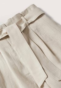 Beżowy detal paska z lnu z kokardą w talii, z plisami i gładkim, teksturowanym materiałem.