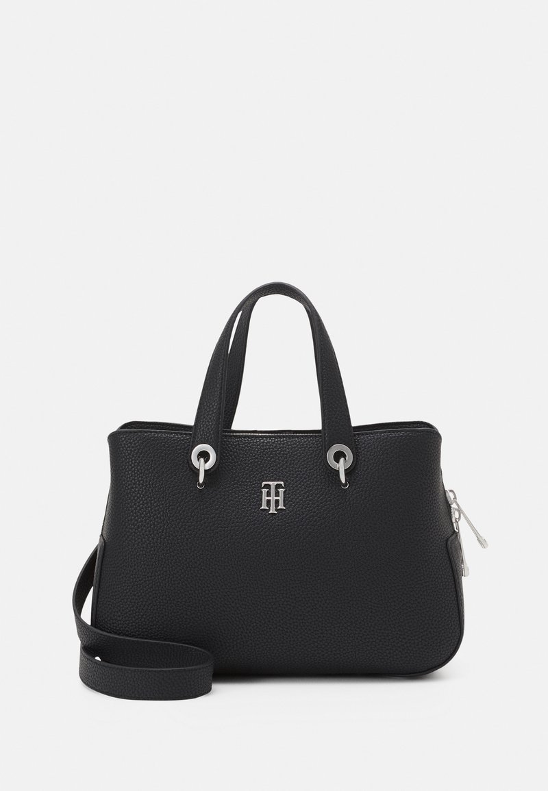 Sac à main en cuir noir texturé avec doubles poignées, emblème logo argenté, fermeture éclair argentée et bandoulière amovible sur fond blanc.
