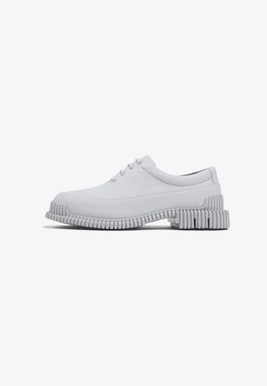 Chaussures en cuir blanc avec semelles en caoutchouc striées. Design à bout arrondi avec cinq œillets et accents de couture minimalistes. Texture lisse dans l'ensemble.
