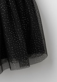 Černá tylová sukně s stříbrnými puntíky, vrstvený design a průhledná textura, s lemem, který končí těsně nad okrajem.