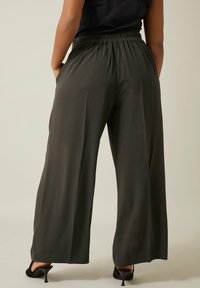 Wijde broek van donkergrijs stof met een elastische tailleband. Heeft zijzakken en een gladde textuur.