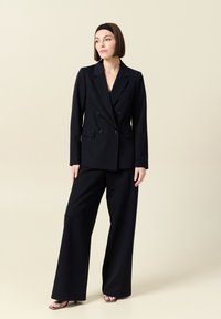 Blazer doppiopetto a righe nere abbinato a pantaloni a gamba larga, con spalle strutturate e rever classici. Tessuto di finitura liscia.
