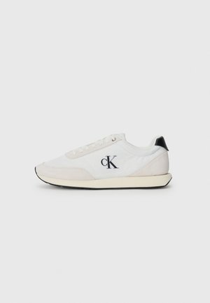 Sneaker bianco realizzato con materiali in suede e tessuto. Presenta un accento nera sul tallone, design con lacci e un piccolo logo nero sul lato.