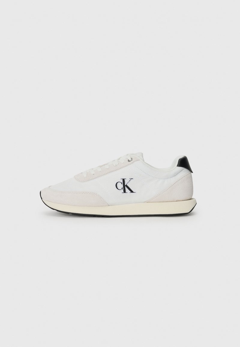 White sneaker with suede and fabric materials. Features a black heel accent, lace-up design, and a small black logo on the side.