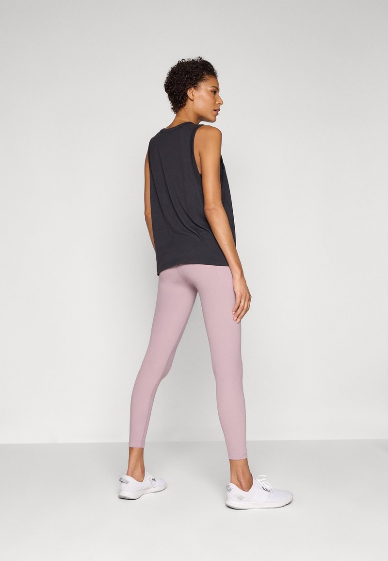Haut noir sans manches sur des leggings roses clairs. Le haut a une coupe décontractée, tandis que les leggings sont ajustés avec une texture lisse. Des baskets blanches complètent la tenue.
