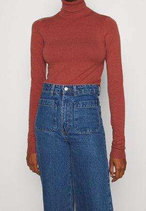 Pull col roulé en rouille, en tissu doux. Associé à un jean en denim bleu taille haute, avec deux poches avant et une fermeture à bouton.