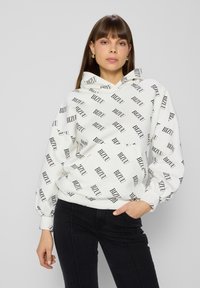 Witte hoodie met zwart "BIZUU" tekstpatroon, trekkoordcapuchon, lange mouwen en een voorzak. Gekozen in combinatie met zwarte strakke broek.