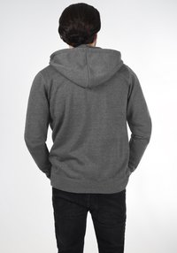 Grijze hoodie met een trekkoordcapuchon en geribde manchetten, weergegeven vanuit de achterkant. Stof lijkt zacht met een gladde textuur. Draagt met zwarte broek.