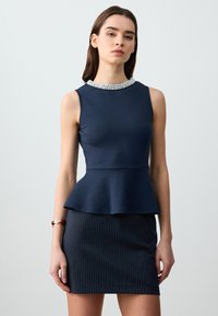 Top peplum blu navy con colletto decorato di perline, abbinato a una gonna a righe aderente. Tessuto morbido con una silhouette strutturata e taglio a ginocchio.