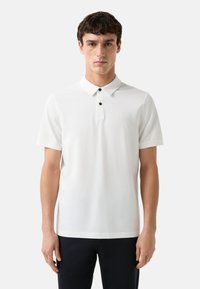 Witte polo met een zachte stof, voorzien van een klassieke kraag, drie zwarte knopen, korte mouwen en een klein merklogo op de borst.