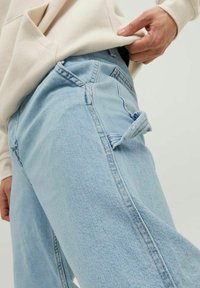 Ljust blå denimjeans med en avslappnad passform, med synliga sömnadsdetaljer och en liten ögla på sidofickan.