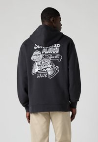 Sweatshirt preta com capuz ajustável, apresentando uma estampa gráfica branca nas costas que inclui uma personagem e o texto "Servindo Sabor".
