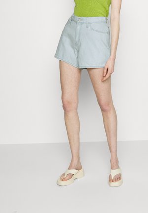 Shorts de denim azul claro de cintura alta, con un cierre frontal clásico de botones y dobladillos limpios. Combinados con sandalias de plataforma beige.