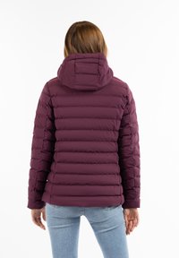 Geacă de umplutură burgundă cu guler înalt și glugă, având secțiuni quilted orizontale și manșete elastice, asortată cu blugi albaștri deschisi.