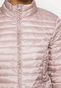 Light pink, quilted puffer jacket with a high collar and full front zipper. Features horizontal seams and a shiny, smooth texture.