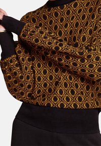 Strickpullover in Schwarz und Senfgelb mit ovalem Muster. Verfügt über lange Ärmel und einen schwarzen Rippbund für eine enge Passform.