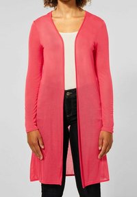 Kevyt, läpikuultava, pitkähihainen neulejakku kirkkaan pinkkinä, avoimella edustalla. Yhdistetty kermaiseen topiin ja tummiin farkkuihin. Sileä kangaspinta.