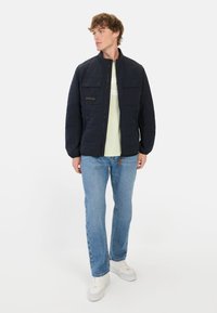 Granatowa pikowana kurtka z stójką, dwoma kieszeniami na piersi i zamkiem błyskawicznym z przodu. Noszona na jasną zieloną koszulę i niebieskie dżinsy. Białe trampki.