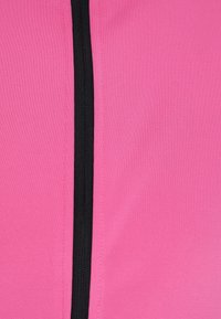 Top sportivo fucsia con cerniera nera al centro, realizzato in tessuto sintetico liscio con superficie texturizzata.