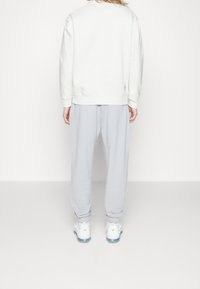 Vit sweatshirt med ribbade ärmar, kombinerad med ljusgråa mjukisbyxor. Anmärkningsvärda vita sneakers med gula accenter och en genomskinlig sula.