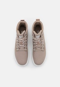 Paire de baskets montantes beige avec semelles blanches et lacets gris clair vues de dessus sur un fond uni.