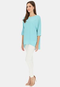 Jasnoniebieska bluzka z rękawami do łokcia, luźny krój i asymetryczny dół, zestawiona z białymi obcisłymi dżinsami i cielistymi szpilkami.