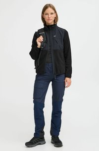 Juodas fleece sportinis švarkas su mėlynomis detalėmis, užtrauktuku užsegamomis kišenėmis, derinamas su tamsiai mėlynomis kargo kelnėmis, turinčiomis kišenių ir juodomis akcentais. Tvirti juodi batai.