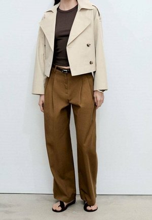 Personne portant une veste courte beige à double boutonnage, un top marron foncé, un pantalon large marron taille haute et des sandales noires ouvertes à l’avant.
