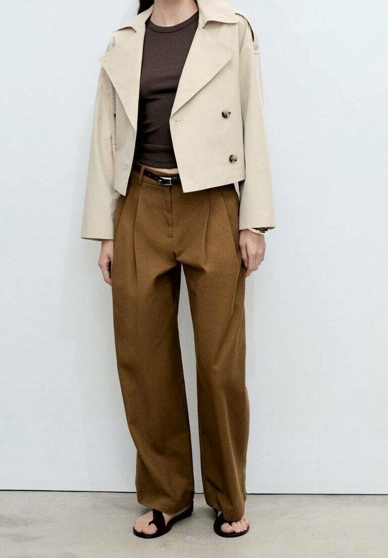 Personne portant une veste courte beige à double boutonnage, un top marron foncé, un pantalon large marron taille haute et des sandales noires ouvertes à l’avant.