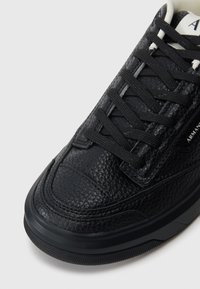 Μαύρο δερμάτινο αθλητικό παπούτσι με υφασμένη επιφάνεια, μαύρες κορδόνες και λάστιχο σόλα. Διαθέτει μια διακριτική λεπτομέρεια λογότυπου στο πλάι. Κλασικός σχεδιασμός.