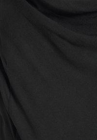 Svart tyg med mjuka veck och synlig stickad struktur, vilket skapar milda skuggor och kurviga linjer.