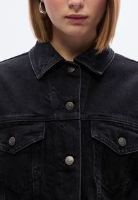 Μαύρο τζιν μπουφάν με γιακά, ασημί κουμπιά snap και δύο τσέπες στο στήθος. Το ύφασμα έχει ελαφριά υφή, παρουσιάζοντας ένα κλασικό σχέδιο.