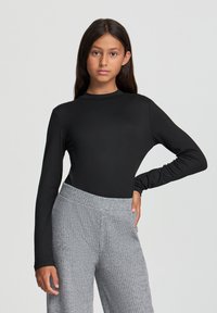 Body a maniche lunghe nera con collo alto; abbinato a pantaloni larghi grigi con texture realizzati in un morbido tessuto a coste.