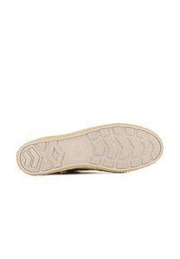 Semelle de chaussure en caoutchouc beige avec un motif de grip texturé, featuring diverses formes géométriques et un logo circulaire au centre.