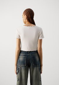 Top bianco tagliato con strisce rosa, texture a coste, orlo scalloped, abbinato a pantaloni cargo in denim scuro a vita alta con tasche a ribalta.