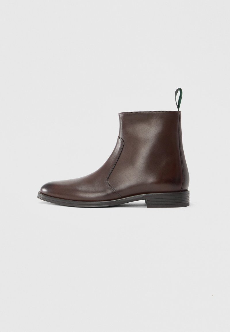 Brauner Leder-Stiefelette mit glatter Oberfläche, ausgestattet mit einem grünen Zuglaschen und einem niedrigen, gestapelten Absatz. Schlankes Design mit seitlichen Elastikeinsätzen.