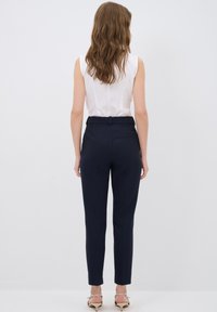 Pantaloni navy con design su misura, texture liscia e vestibilità slim. Presentano una cintura con passanti per la cintura e tasche posteriori.