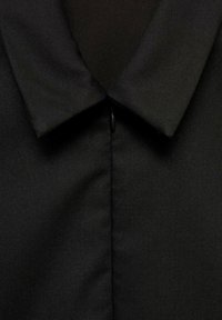 Cămașă neagră cu guler, având o textură netedă, țesută. Dispune de un închidere frontală și un design minimalistic, cu linii clare.