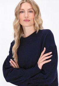 Granatowy sweter z dzianiny z okrągłym dekoltem, długimi bufkami i ściągaczami. Gładka tekstura podkreśla miękki materiał.