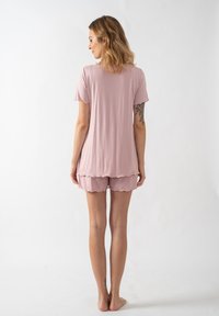 Světle růžový set pyžama obsahující tričko s krátkým rukávem a krajkové šortky. Měkká, hladká tkanina s volným střihem a vlnitými okraji.