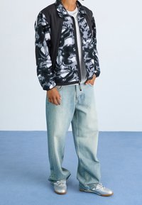 Chaqueta bomber de tie-dye en blanco y negro sobre una camiseta gris, combinada con unos vaqueros light blue holgados y zapatillas plateadas.